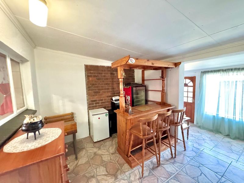 A dedicated bar area featuring a built-in wooden bar counter, exposed brickwork, and durable tiled flooring, offering a functional space for entertaining.