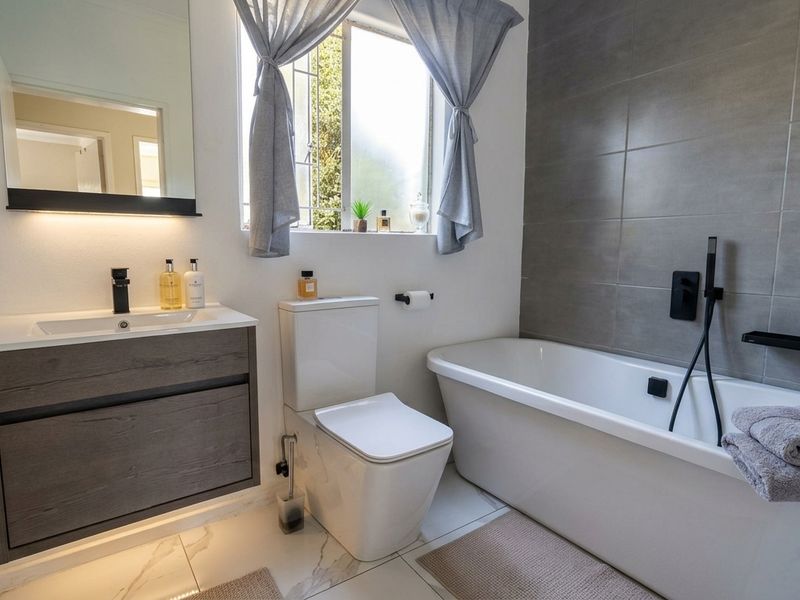 Modern bathroom featuring a floating vanity, freestanding bathtub with black fixtures, and contemporary grey wall tiling.