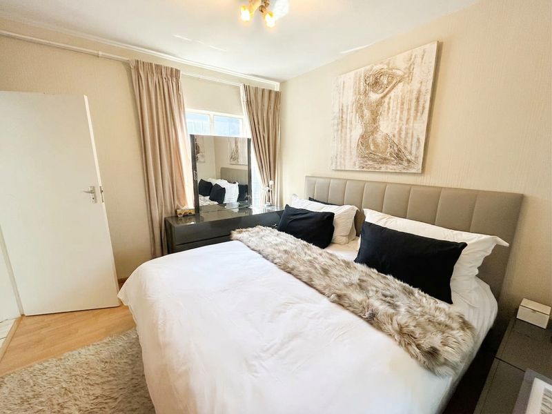 A well-maintained bedroom featuring laminate flooring, neutral wall finishes, and a window with curtains.