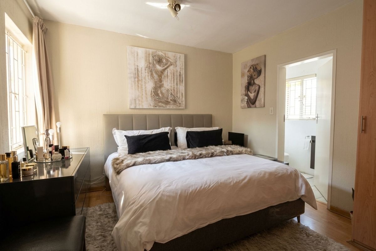 A well-lit bedroom featuring laminate flooring, a built-in wardrobe, and an adjoining en-suite bathroom.