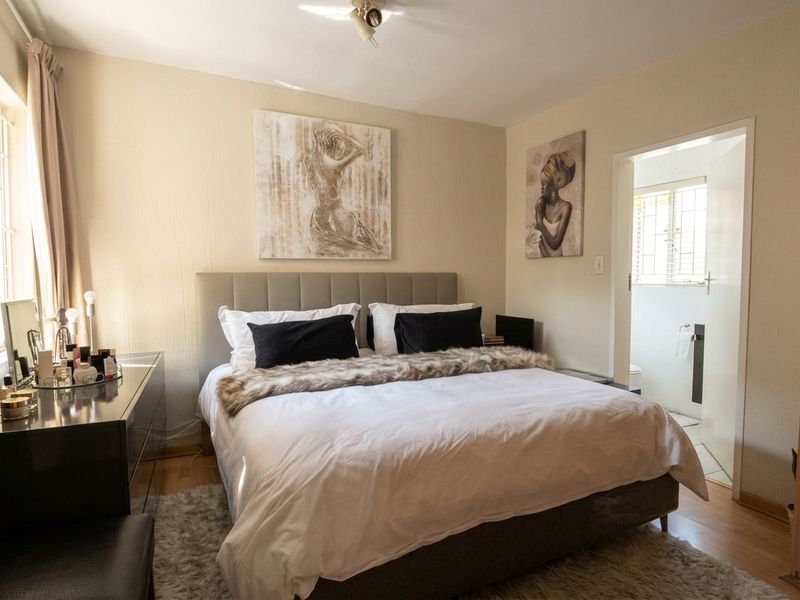 A well-lit bedroom featuring laminate flooring, a built-in wardrobe, and an adjoining en-suite bathroom.