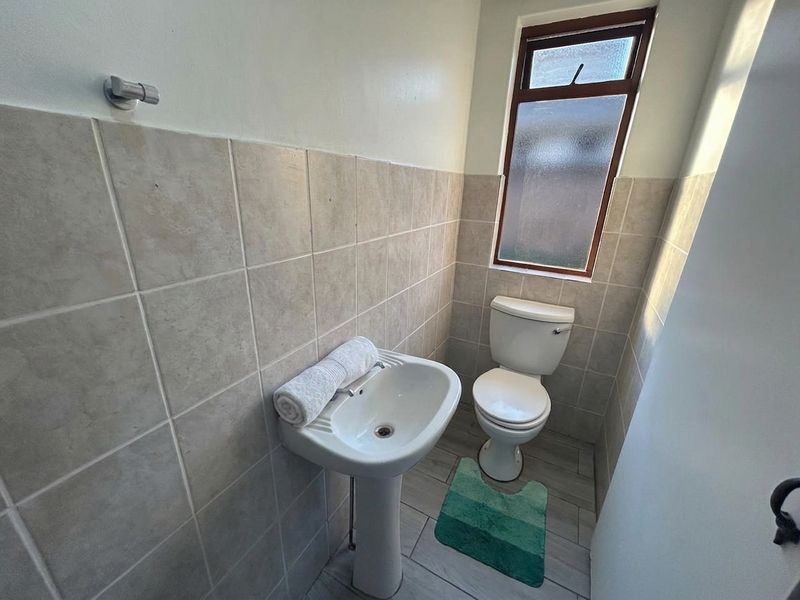 A compact bathroom featuring a pedestal basin, toilet, neutral wall tiling, and an obscured glass window for privacy.