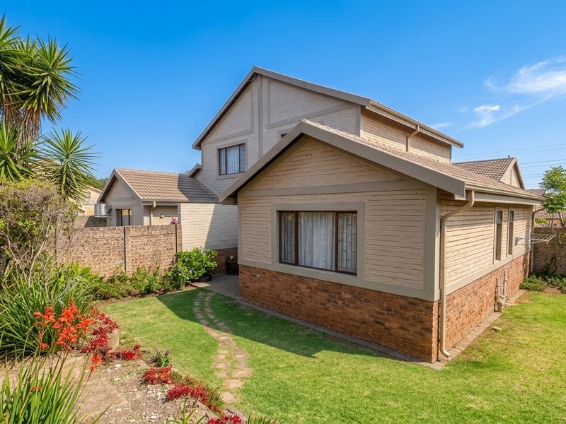 Rear view of the townhouse featuring a well-maintained garden, brick and cladding exterior, tiled roof, and a paved pathway leading through the lawn.