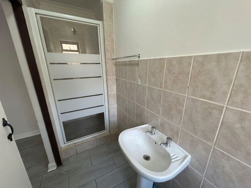 A functional bathroom featuring a pedestal basin, tiled splashback, and a glass-enclosed shower unit with frosted detailing.