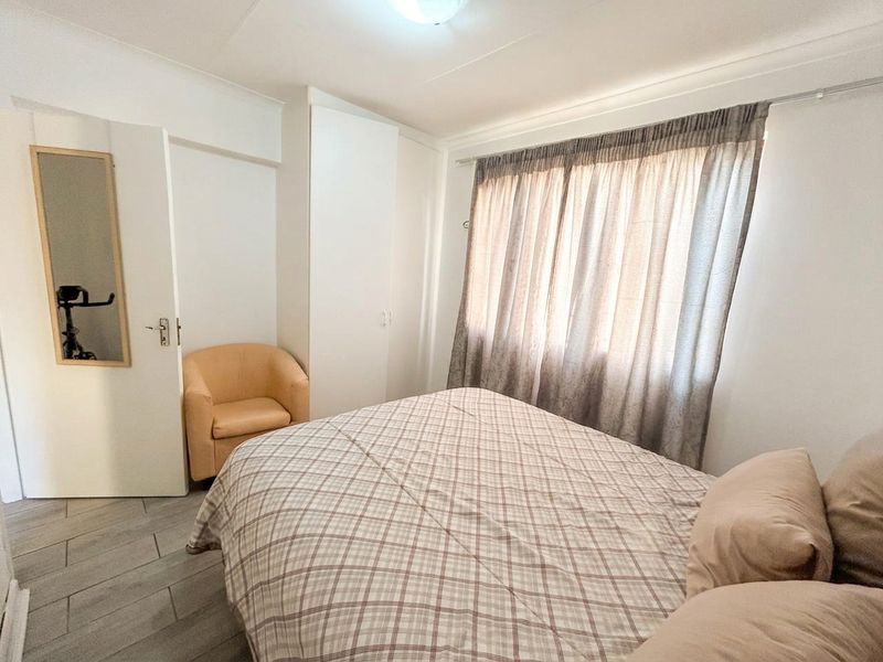 A functional bedroom featuring built-in cupboards, tiled flooring, and neutral finishes, offering a clean and simple space ready for personalization.