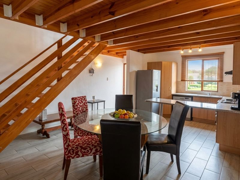 Open-plan living and kitchen area featuring exposed timber ceiling beams, a wooden staircase, and functional kitchen cabinetry with tiled flooring throughout.