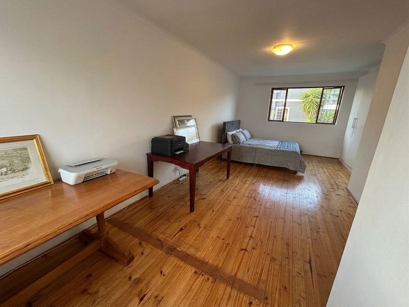 Spacious bedroom featuring polished timber flooring, built-in storage cupboards, and natural light through a window.
