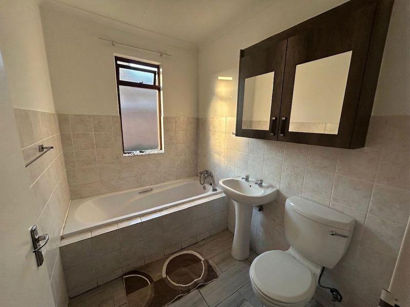 A functional bathroom featuring a bathtub, pedestal basin, toilet, and wall-mounted storage cabinet with tiled finishes throughout.