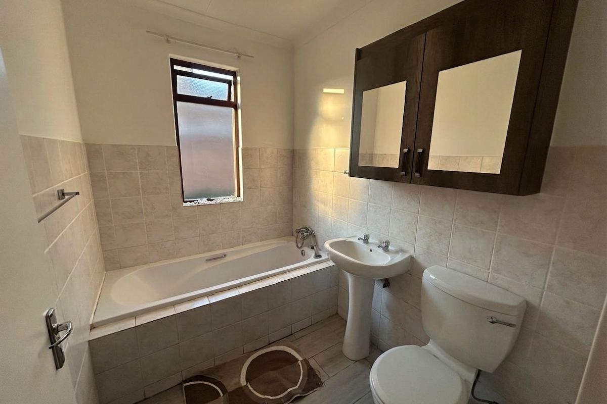 A functional bathroom featuring a bathtub, pedestal basin, toilet, and wall-mounted storage cabinet with tiled finishes throughout.