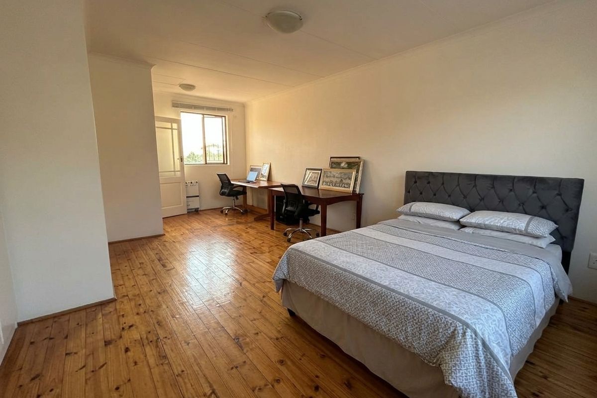 Spacious bedroom featuring polished timber flooring and natural light, offering a versatile layout suitable for a sleeping area and integrated home office space.