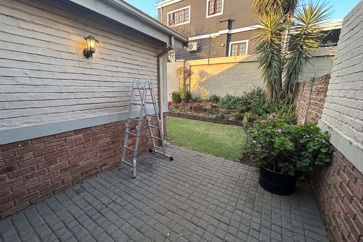 A private rear courtyard featuring a paved patio area, a small lawn, and tiered garden beds enclosed by brick boundary walls.