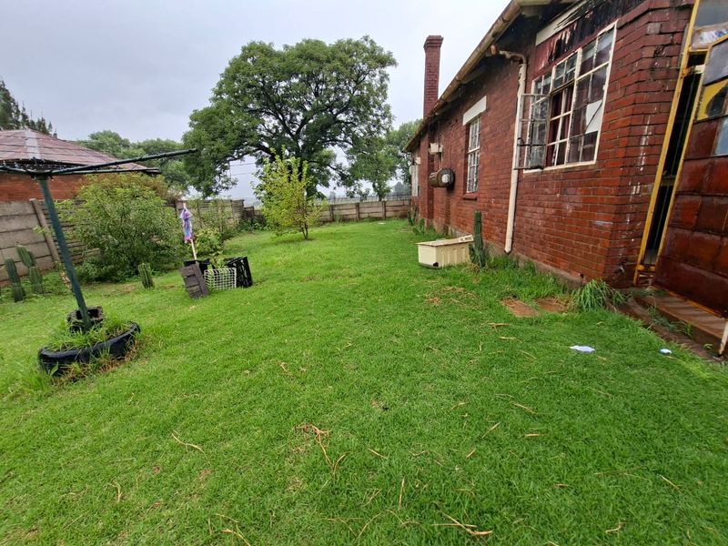 Rear exterior view of a brick house featuring a large garden, chimney, and steel-framed windows, requiring maintenance and landscaping.