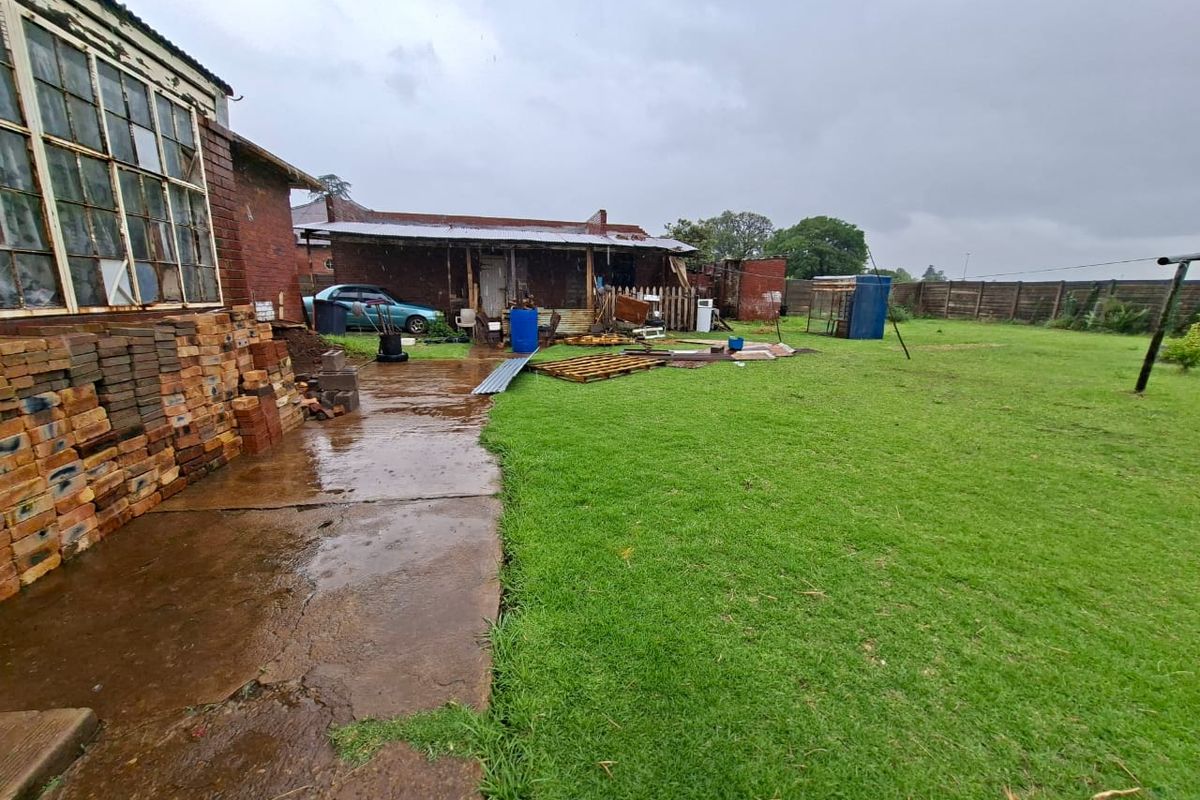 Rear exterior view of the property showing a concrete patio, brick structure, and large garden area requiring significant maintenance and repair.