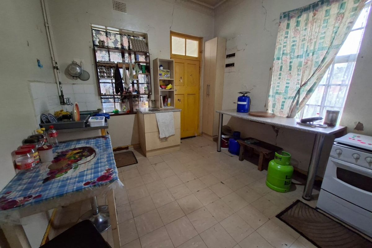 A dated kitchen featuring tiled flooring, basic cabinetry, and a freestanding stove, requiring significant cosmetic updates and repairs to wall finishes.