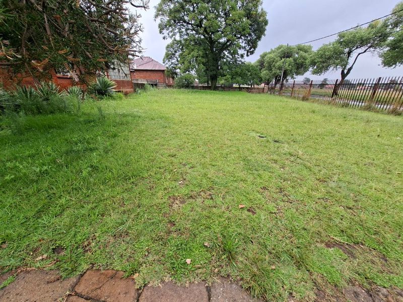 A spacious, open garden area featuring mature trees and metal perimeter fencing, offering significant potential for landscaping and outdoor development.