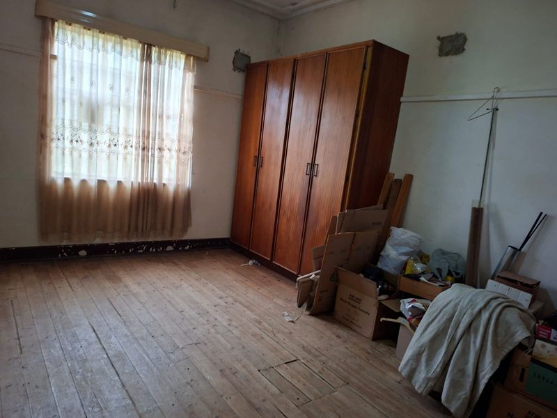 A bedroom featuring original timber flooring, a built-in wardrobe, and a picture rail, currently requiring cosmetic updates and repairs to the walls and skirting.