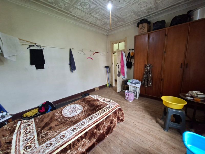 A bedroom featuring original ornate pressed metal ceilings, timber flooring, and a built-in wardrobe, currently requiring cosmetic updates and refurbishment.