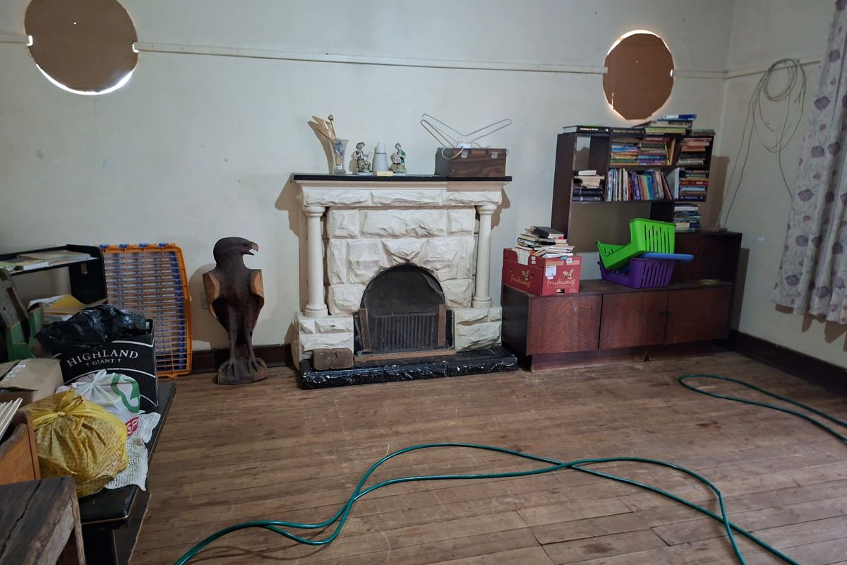 Living room featuring a stone fireplace, timber flooring, and unique circular windows, currently requiring significant maintenance and cosmetic updates.