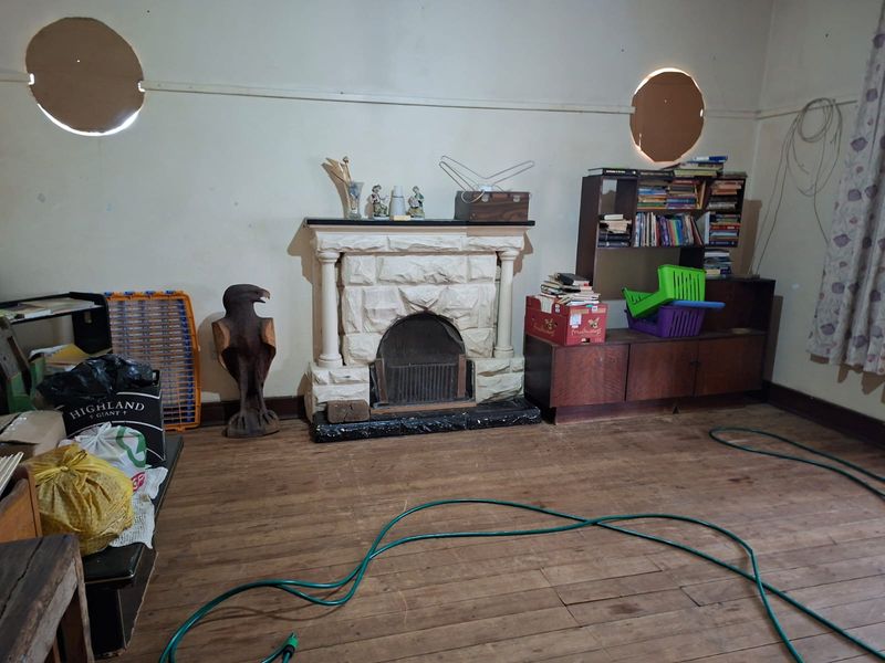 Living room featuring a stone fireplace, timber flooring, and unique circular windows, currently requiring significant maintenance and cosmetic updates.