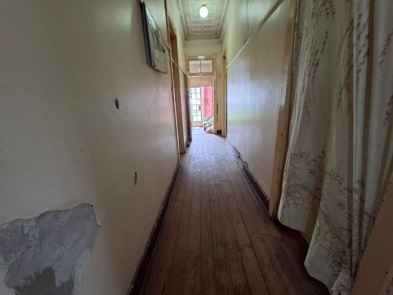 A long hallway featuring original timber flooring and a pressed metal ceiling, currently requiring significant cosmetic repairs and refurbishment to restore its character.