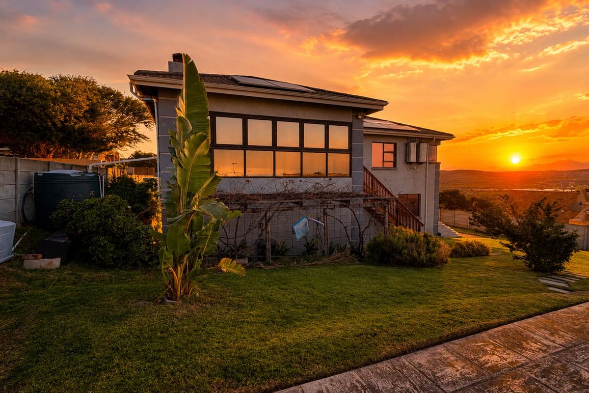 Rear view of the house at sunset, featuring a landscaped garden, paved walkway, solar panels, and a water tank.