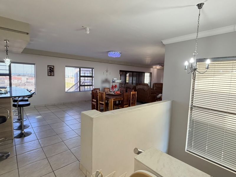 Spacious open-plan living and dining area featuring tiled flooring, a breakfast bar, and large windows with venetian blinds.