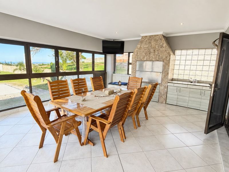 Spacious enclosed patio featuring a built-in braai, stone cladding, tiled flooring, and large aluminium sliding doors offering expansive garden and coastal views.