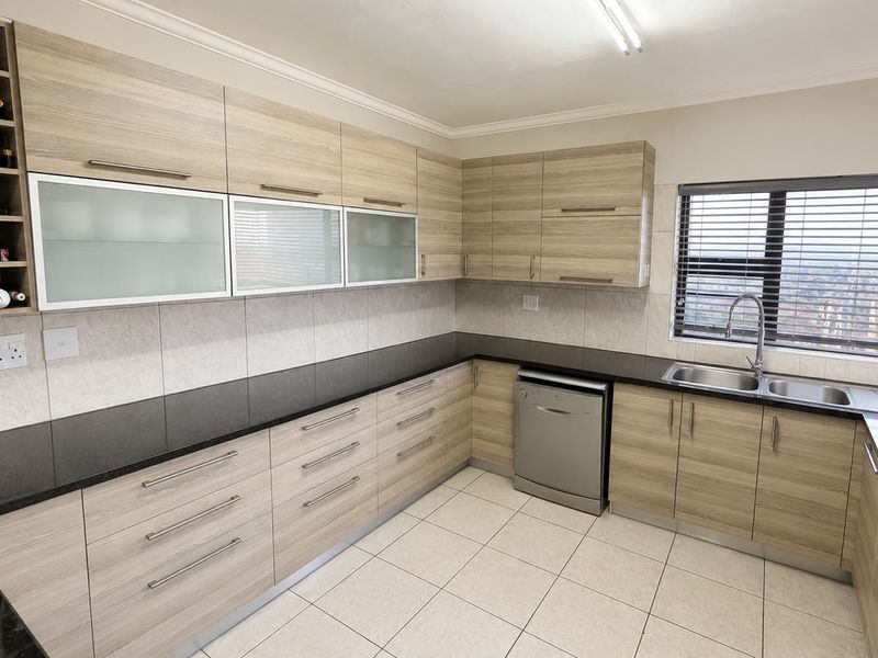 Modern kitchen featuring light wood-grain cabinetry, integrated dishwasher, double basin sink, and a built-in wine rack with neutral tiled flooring and backsplash.