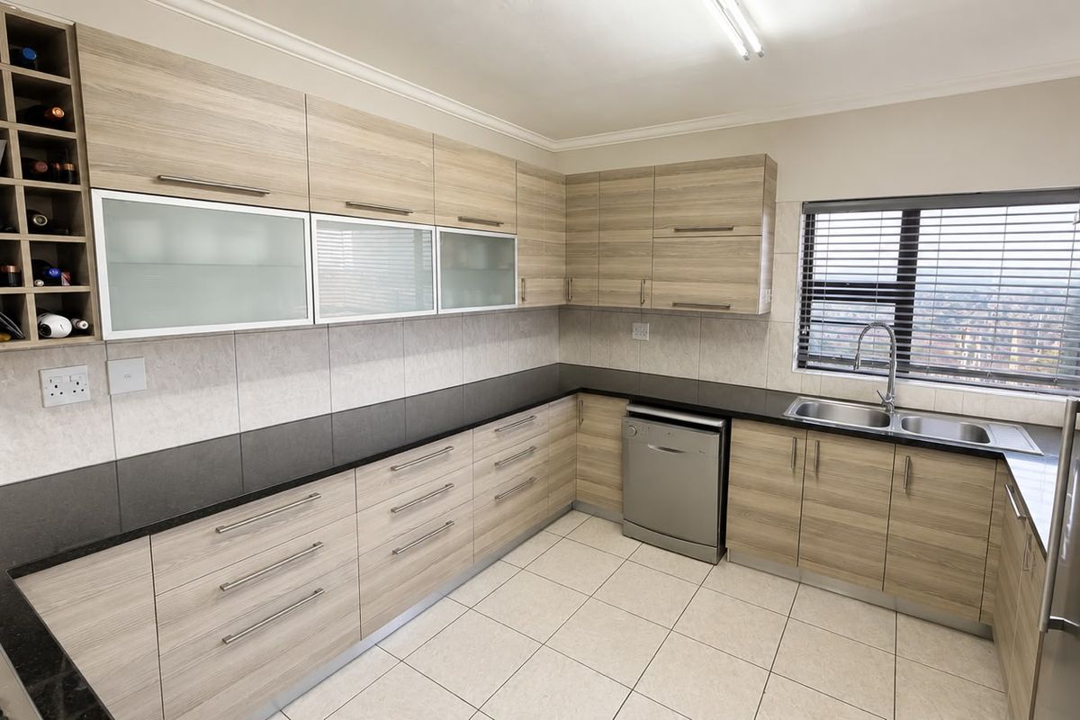 Modern kitchen featuring light wood-grain cabinetry, integrated dishwasher, double basin sink, and a built-in wine rack with neutral tiled flooring and backsplash.