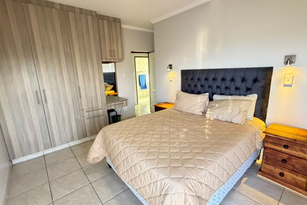 A well-maintained bedroom featuring built-in wooden cupboards, tiled flooring, and direct access to an en-suite bathroom.