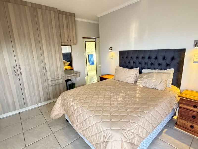 A well-maintained bedroom featuring built-in wooden cupboards, tiled flooring, and direct access to an en-suite bathroom.