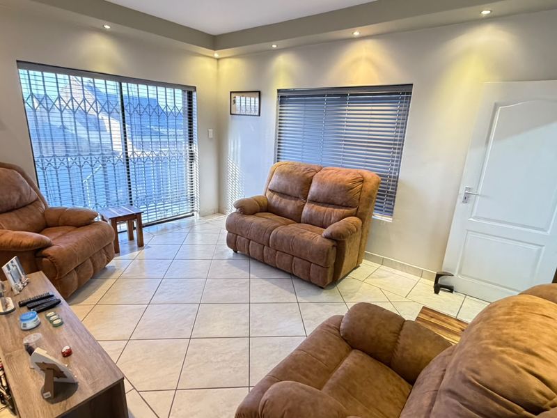 A bright living room featuring tiled flooring, recessed downlighting, and large sliding doors with security gates leading to the exterior.