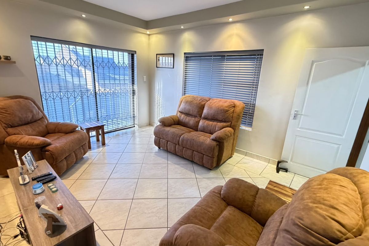 A bright living room featuring tiled flooring, recessed downlighting, and large sliding doors with security gates leading to the exterior.