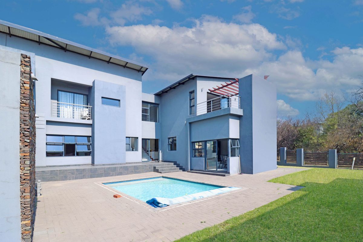 Rear view of a modern double-story house featuring a swimming pool, paved patio area, balcony, and stone-clad exterior wall.