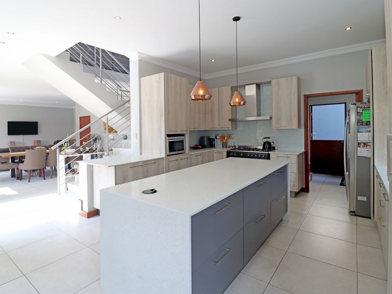Modern open-plan kitchen featuring a large central island with quartz countertops, integrated appliances, and a sleek staircase leading to the upper level.