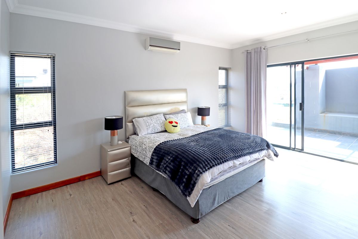 A well-maintained bedroom featuring laminate flooring, an air conditioning unit, and sliding glass doors providing direct access to an outdoor area.