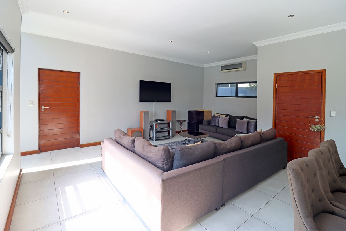 A well-maintained living room featuring tiled flooring, recessed downlights, an integrated air conditioning unit, and modern wooden doors.