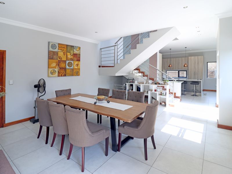 Spacious open-plan dining and kitchen area featuring modern tiled flooring, a central staircase with stainless steel balustrades, and contemporary kitchen cabinetry.