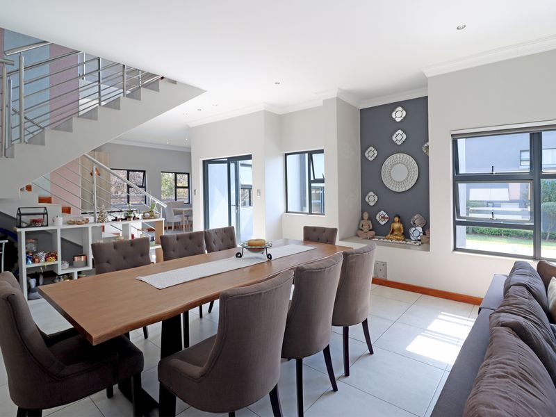 Spacious open-plan dining area featuring tiled floors, a modern staircase with stainless steel balustrades, and large windows providing ample natural light.