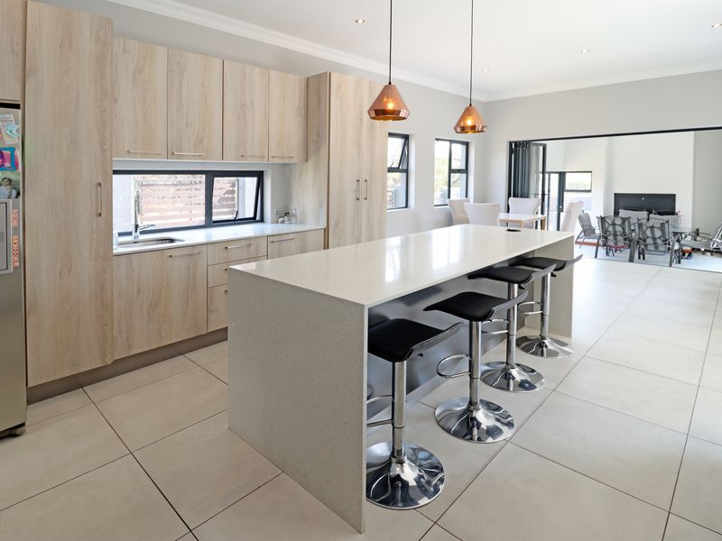 Modern open-plan kitchen featuring light wood cabinetry, a large quartz island with breakfast bar seating, and seamless flow to the adjacent living area.