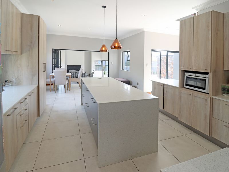 Modern kitchen featuring a large central island with quartz countertops, light wood cabinetry, built-in oven, and stylish pendant lighting, flowing into the dining area.