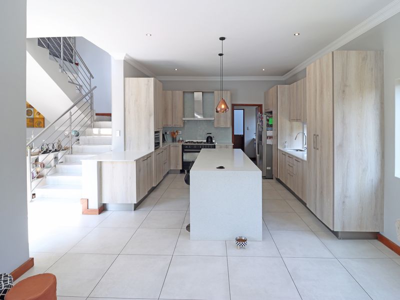 Modern open-plan kitchen featuring light wood cabinetry, quartz countertops, a central island, and a sleek staircase with a stainless steel balustrade.