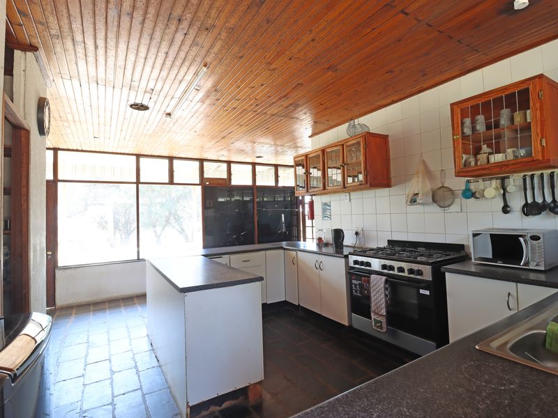 A functional kitchen featuring a gas stove, ample cabinetry, tiled flooring, and a timber-clad ceiling with large windows providing natural light.