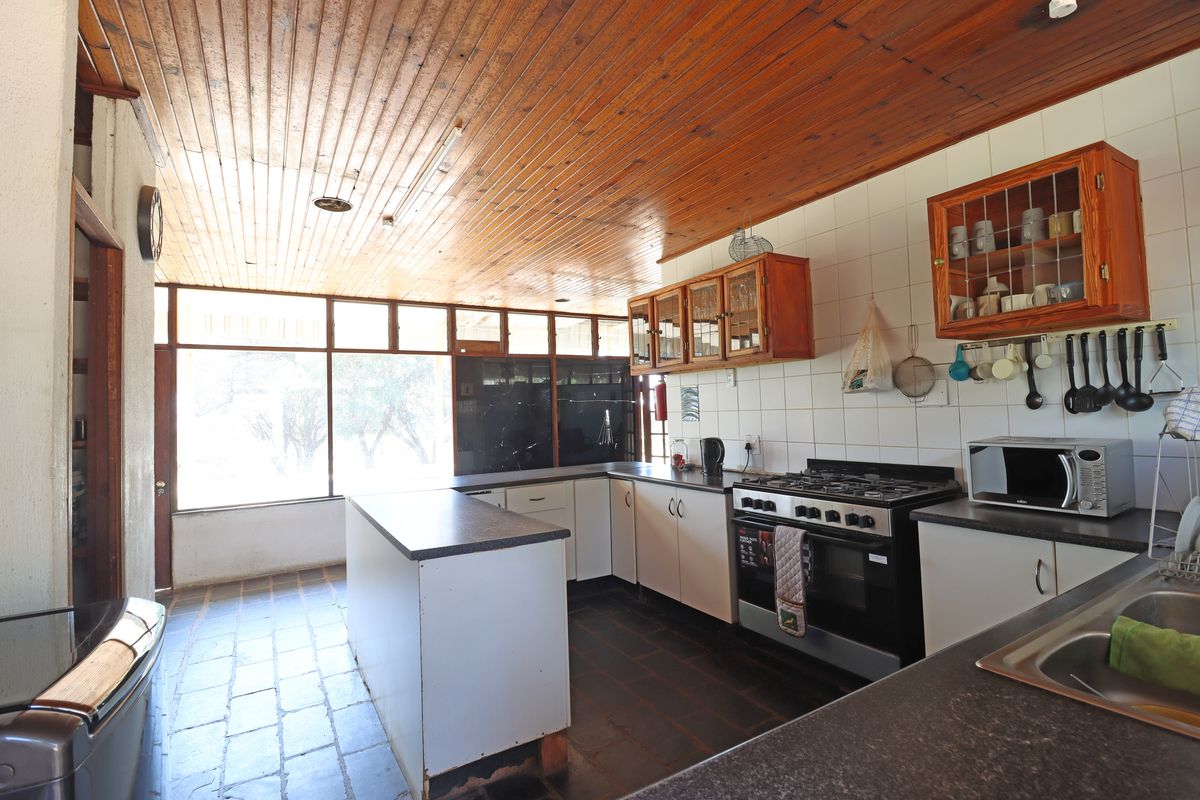 A functional kitchen featuring a gas stove, ample cabinetry, tiled flooring, and a timber-clad ceiling with large windows providing natural light.
