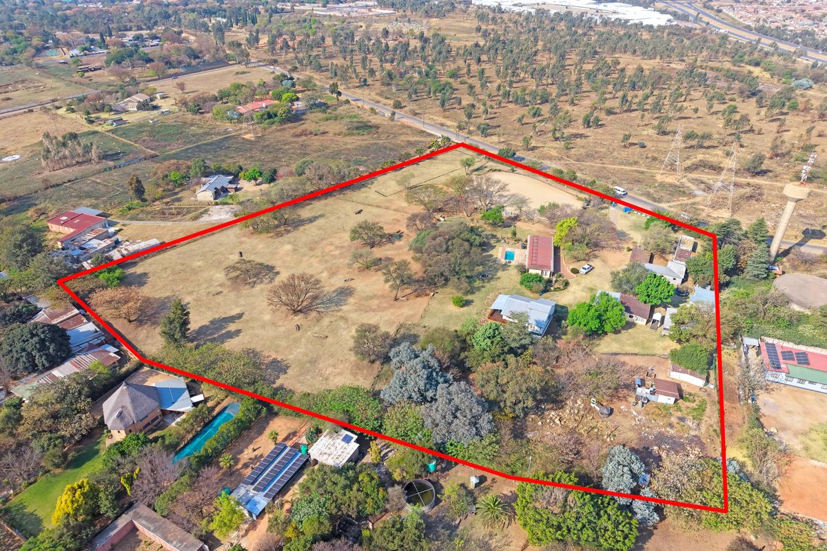Aerial view of a large farm property featuring multiple structures, a swimming pool, solar installations, and extensive open land within a marked boundary.
