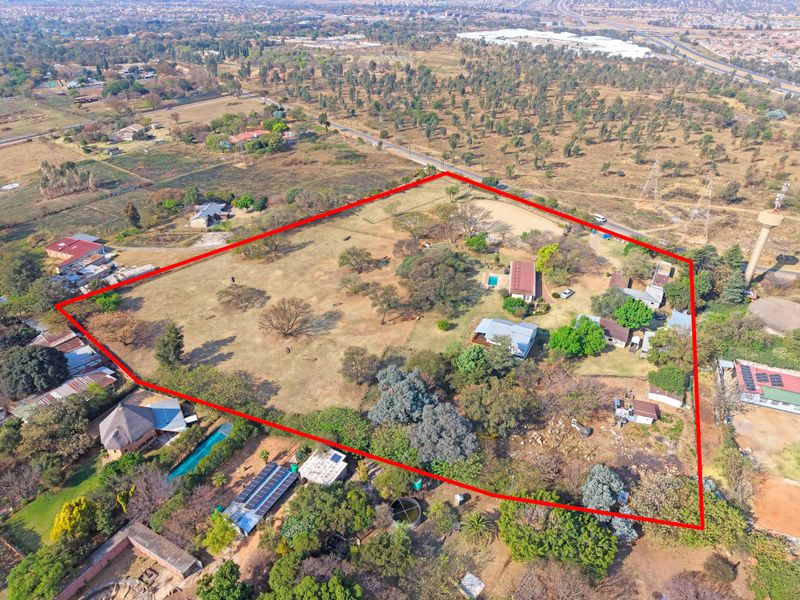 Aerial view of a large farm property featuring multiple structures, a swimming pool, solar installations, and extensive open land within a marked boundary.