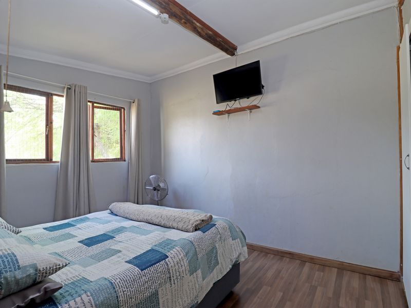 A functional bedroom featuring laminate flooring, an exposed timber ceiling beam, and built-in wardrobe storage with natural light from timber-framed windows.