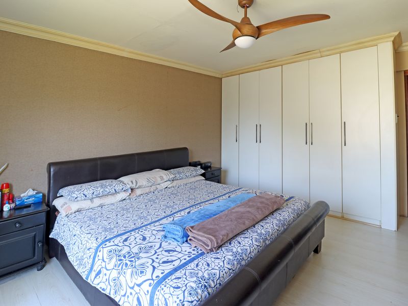 A bedroom featuring built-in cupboards, a ceiling fan, and laminate flooring, providing a functional and neutral space.