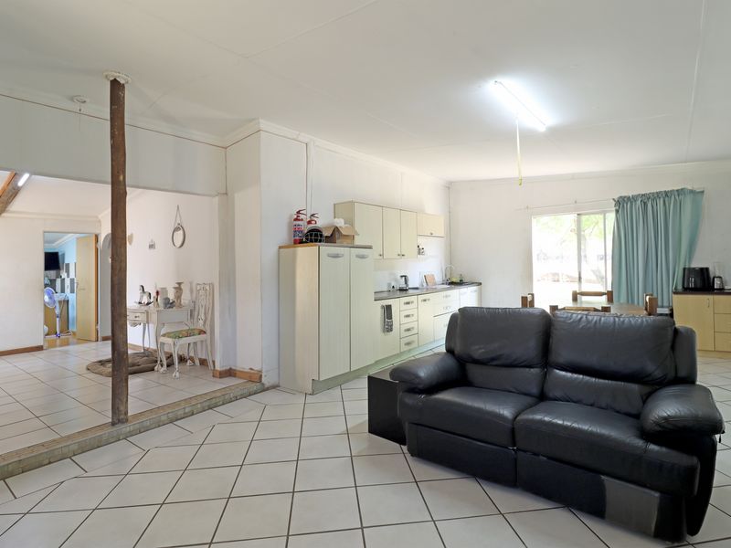 Open-plan living and kitchen area featuring tiled flooring, dated cabinetry, and a central support column, offering a functional layout with potential for modernization.