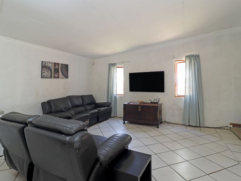 A living room featuring tiled flooring and wall-mounted television, requiring cosmetic updates to the wall finishes.